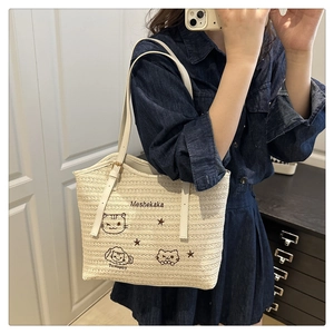Detail of embroidered cat pattern on beige woven tote bag worn by model in denim
