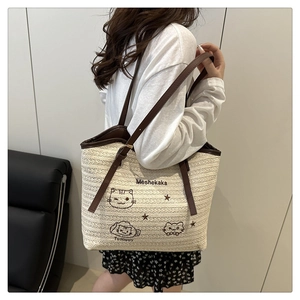 Detail of cream woven tote bag featuring cute cat embroidery and brown leather strap