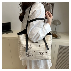 Detail of woven tote bag featuring cat embroidery and contrasting black shoulder straps