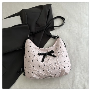 Détail de la texture plissée rose du sac cabas avec nœud noir et pendentif cœur argenté