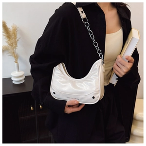 Detail of cream glossy patent crescent bag with silver chain and side stud accents