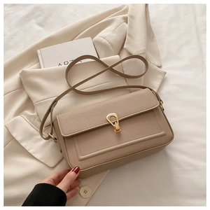 Détail du sac à bandoulière beige avec texture litchi et fermoir doré sur fond de costume