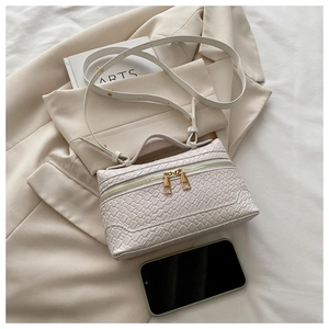 Detail of white woven texture crossbody bag with double gold zippers on a beige blazer