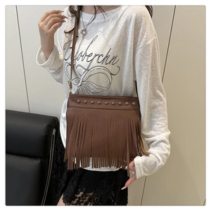 Détail d'un sac bandoulière en cuir marron avec des clous argentés et de longues franges