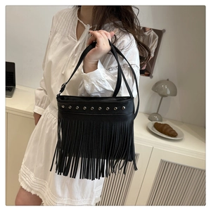 Détail du sac en cuir noir avec clous argentés et longues franges dans un décor de maison