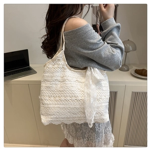 Detailed side view of a white lace woven tote bag with a sheer silk scarf bow on the side