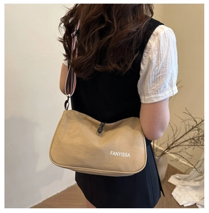 Détail du sac bandoulière en tissu kaki avec large bandoulière rayée et logo blanc