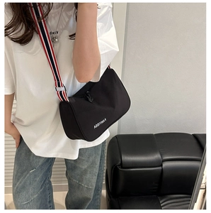 Detail of a black nylon crossbody bag with wide tri-color striped strap and logo