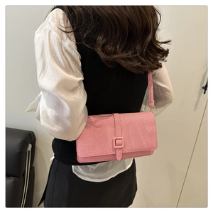 Detail of pink twill crossbody bag with square buckle flap on a model in a minimalist setting