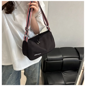 Detail of black canvas messenger bag with a tricolor striped strap and top dual zipper