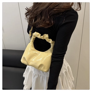 Close-up of cream pleated shoulder bag featuring glossy patent leather and fashion logo