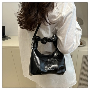 Close-up of black glossy leather hobo bag with pleated handle and fashion typography