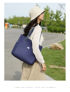 Detail of navy blue nylon tote bag with gray straps and metal plaque on shoulder