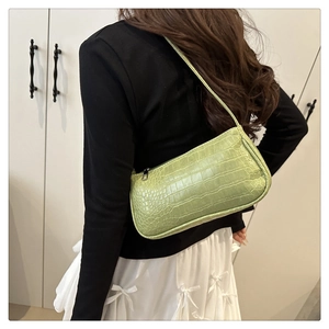 Green crocodile pattern baguette bag worn over the shoulder by a fashion model