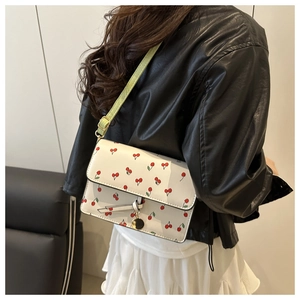 Détail du sac bandoulière blanc à motif cerise porté sur une veste en cuir noir élégante