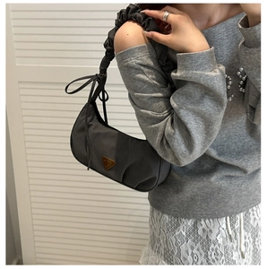 Detail of grey pleated shoulder strap and metallic triangular logo on nylon hobo bag