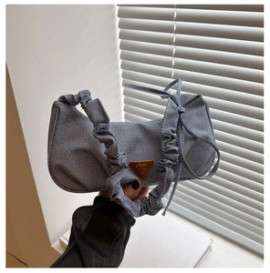 Detail view of denim underarm bag featuring ruched scrunchie handles and metal logo