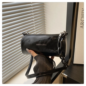 Détail du sac cylindrique noir minimaliste avec bandoulière et chaîne décorative