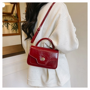Dark red patent leather crossbody bag with gold metal clasp on a textured strap