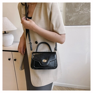 Detail of glossy black leather handbag with a golden rotating metal lock and top handle