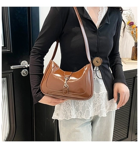 Close-up of a brown glossy leather underarm bag with a vintage metal hook buckle clasp