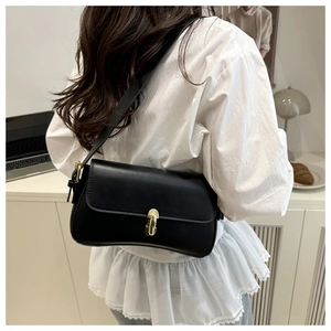 Detail of a chic black leather underarm bag with gold lock worn by a model in white blouse