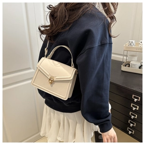 Détail d'un sac à main crème avec fermoir doré porté par un modèle dans un intérieur