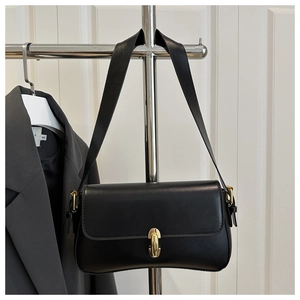 Detail of a black leather flap underarm bag with a bold gold clasp on a metal stand