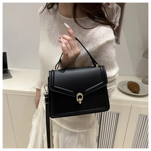 Detail of black crossbody bag featuring a golden double-ring buckle and a sleek V-flap design