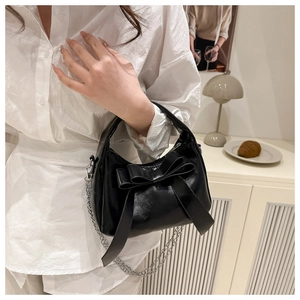 Détail du sac en cuir brillant noir avec grand nœud et bandoulière chaîne argentée