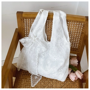 Close-up of white lace tote bag with large bow detail on a vintage wooden chair