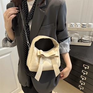 Elegant beige bow handbag with silver chain strap shown in a stylish lifestyle setting