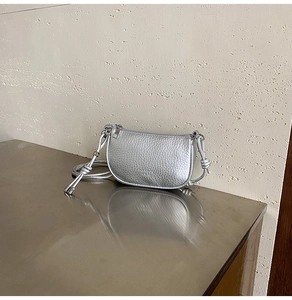 Dettaglio borsa a sella argento con trama litchi e nodi decorativi sulla tracolla