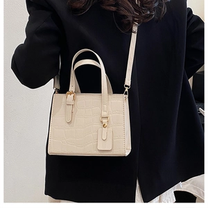 Detail of cream croc-effect leather handbag with gold buckles on black blazer background
