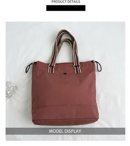 Detail of burgundy tote bag featuring striped handles and a sleek black metal logo