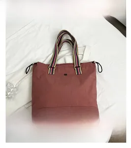 Detail of burgundy tote bag featuring striped handles and a sleek black metal logo