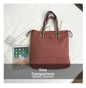 Size comparison of dusty rose nylon tote bag with striped straps next to an iPad