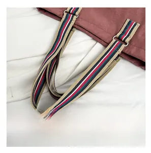 Detail of canvas shoulder bag with colorful striped strap and clover metal ornament