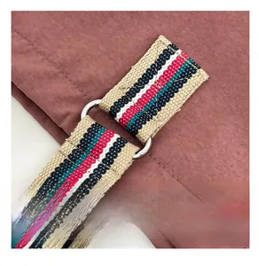 Close-up of pink shoulder bag with striped woven strap and silver metal D-ring attachment