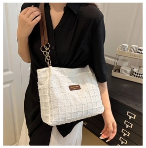 Detailed view of white tweed tote bag with brown leather straps and gold chain accent