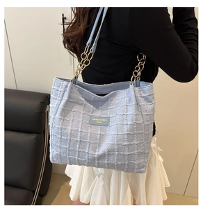 Close-up of light blue tweed tote bag with woven texture and gold chain shoulder strap