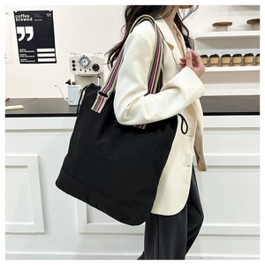 Detail shot of black canvas tote bag with colorful red blue and beige striped handles