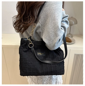 Detail of black textured tote bag featuring gold chain strap and luxury fabric finish
