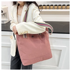 Detail of pink canvas tote bag with multi-color striped strap and clover metal logo
