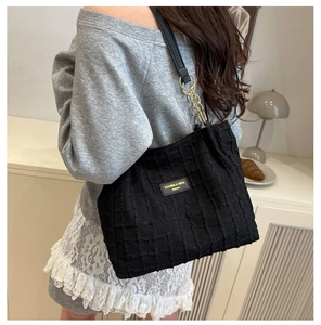 Detail of black textured tote bag with gold chain strap and brand nameplate on shoulder