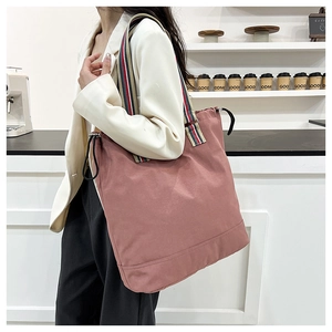 Macro detail of dusty rose tote bag with colorful striped handles and drawstring side