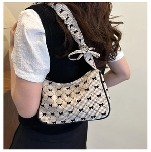 Detail view of beige plaid shoulder bag with black bow prints on model side profile