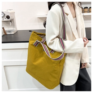 Detail of a large yellow tote bag with colorful striped strap in a cafe setting