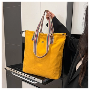 Macro view of bright yellow canvas tote featuring colorful woven straps and metal logo