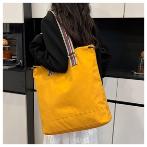 Close-up of a yellow canvas tote bag with striped straps and drawstring details